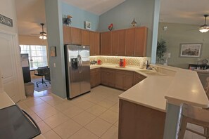 A modern kitchen with wooden cabinets, a stainless steel refrigerator, and a white countertop. - Lakeside Luxury #198 (Rotonda West)