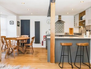 A modern kitchen with a central island, bar stools, and wooden chairs. - Winksey Cottage (Harrogate)