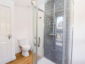 A bathroom with a glass-enclosed shower, a toilet, and a white door. - Winksey Cottage (Harrogate)