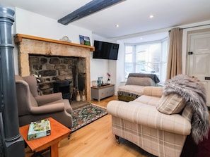 A living room with a stone fireplace, a sofa, a coffee table, and a television mounted on the wall. - Winksey Cottage (Harrogate)