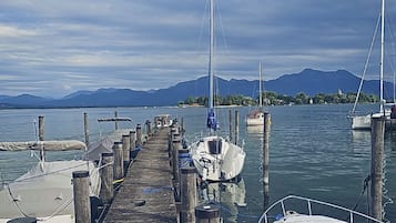 Une jetée en bois mène à une marina où sont amarrés des bateaux. Le ciel est dégagé et on aperçoit des montagnes au loin.