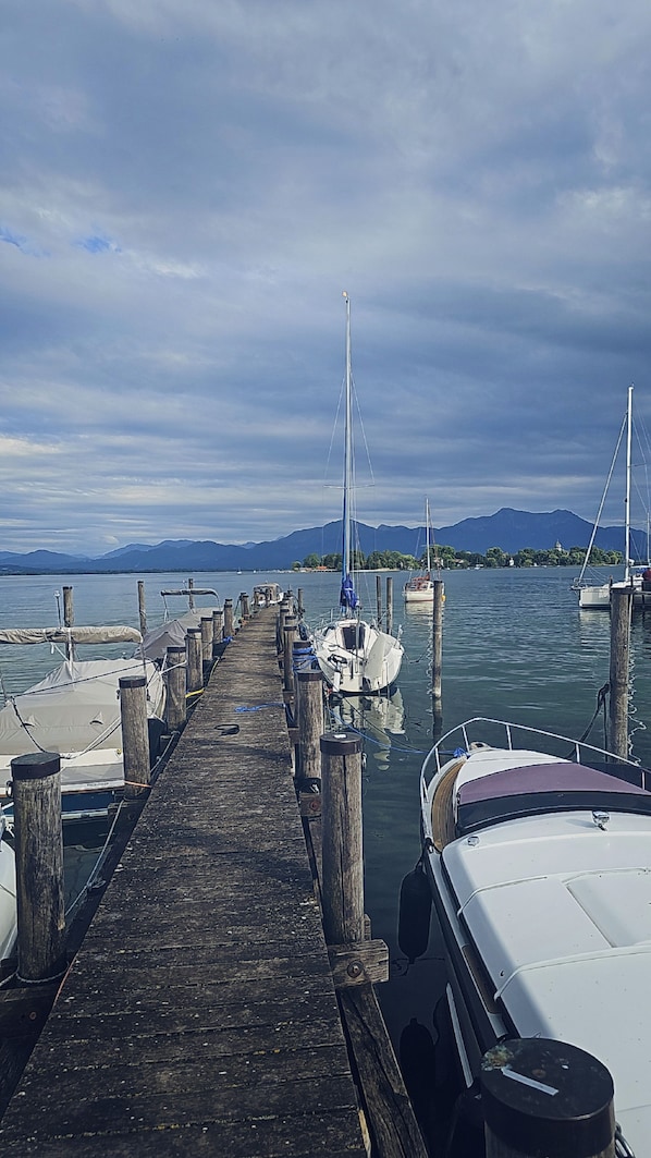 A wooden pier leading to a marina with boats docked, a clear sky, and mountains in the distance.