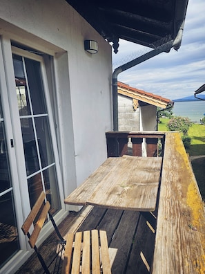 A wooden table and bench on a balcony with a view of a lake and mountains. - Haus am See Fraueninsel (Fraueninsel)