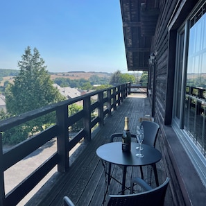 Une terrasse en bois avec une table et des chaises, une bouteille de vin et un verre dessus.