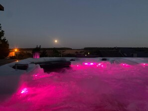 Un toit-terrasse avec un jacuzzi illuminé de lumières roses, entouré de neige, et une vue sur la ville en arrière-plan.