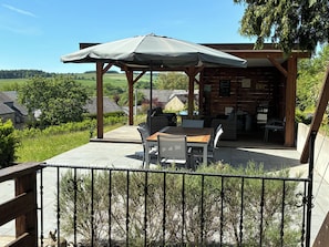 Une terrasse extérieure avec une table et des chaises en bois, un espace salon couvert et une vue sur le paysage environnant.