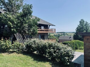 A two-story stone building with a wooden balcony, surrounded by lush greenery and a clear view of the countryside. - Cozy Chalet near Durbuy (Somme-Leuze)