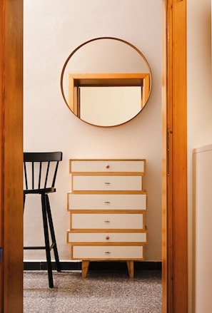 Una stanza con una cassettiera in legno, una sedia e uno specchio rotondo appeso al muro.