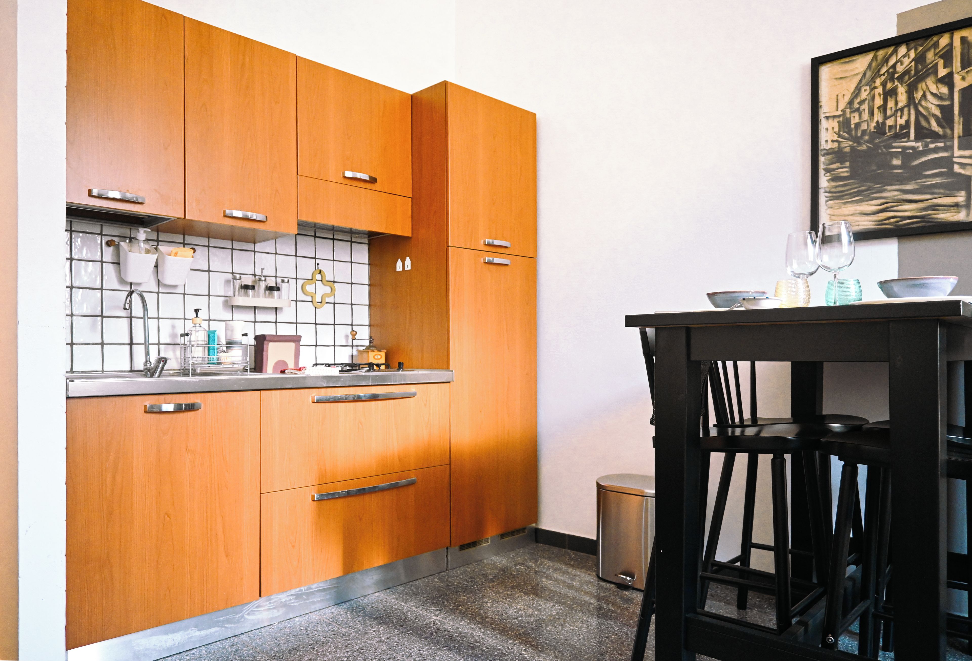 Een keuken met houten kastjes, een betegelde spatwand en een kleine prullenbak.