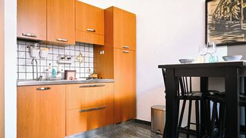 Een keuken met houten kastjes, een betegelde spatwand en een kleine prullenbak.