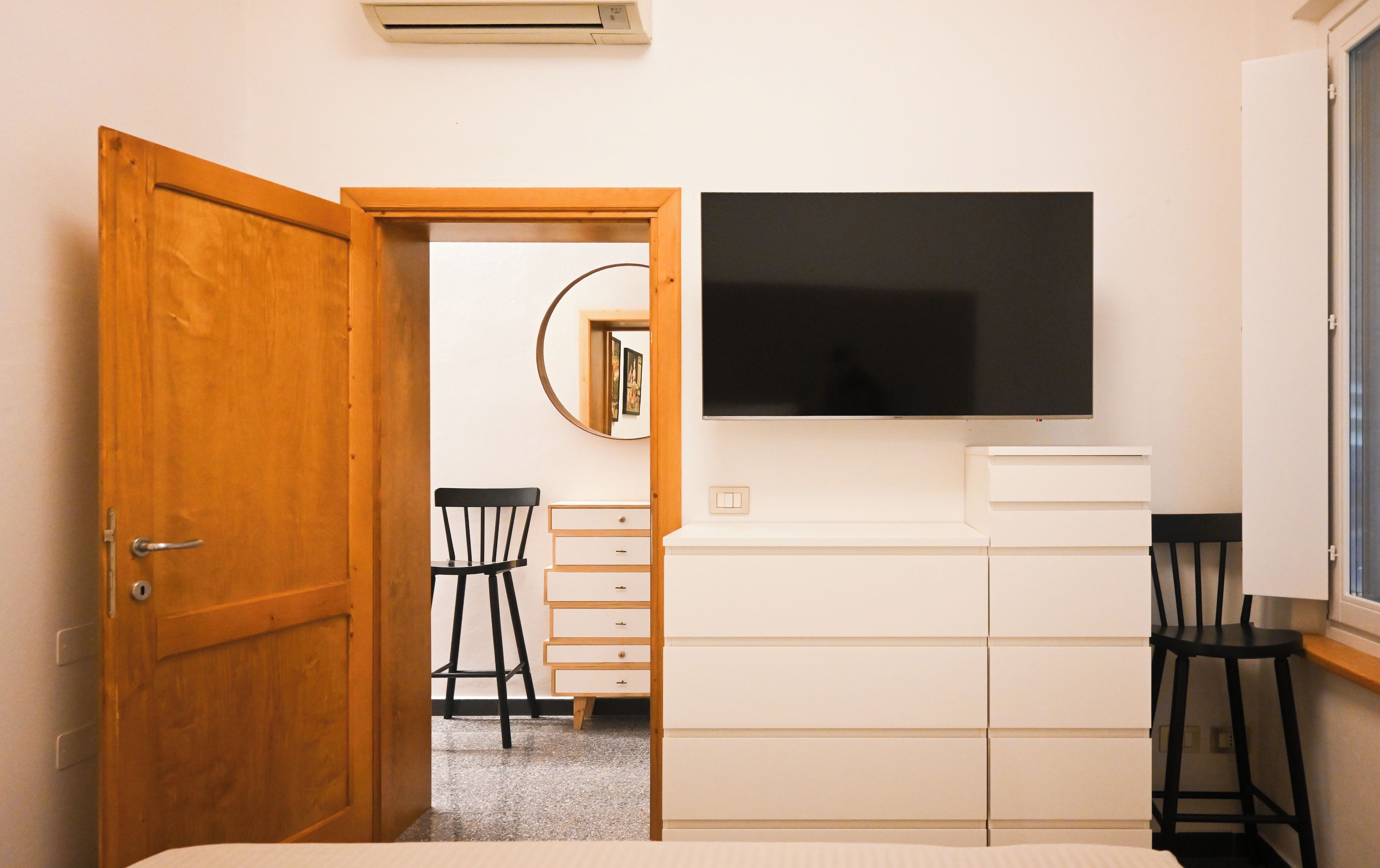 A bedroom with a bed, a dresser, a chair, a television, and a door leading to another room.