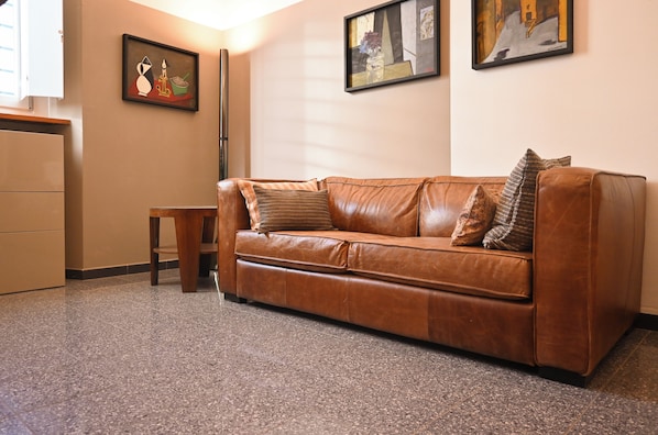 A brown leather sofa with cushions, a small wooden stool, and a framed painting on the wall. - Panciatichi 10 - Careggi - University - Downtown (Firenze)