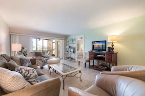 A living room with a sofa set, a glass coffee table, a television, and a lamp. - Siesta Key Beach Escape- 2 BR / 2BA Condo by RVA (Sarasota)