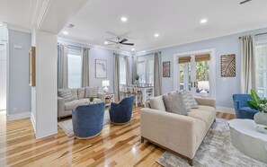 A modern living room with a beige sofa, blue armchairs, and a dining area with a table and chairs. - Chillville: Pool, Playground & Bikes (Santa Rosa Beach)