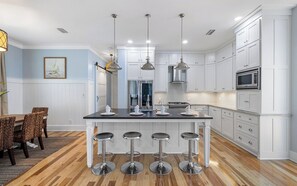 Una cocina moderna con armarios blancos, una isla central con taburetes de bar, electrodomésticos de acero inoxidable e iluminación colgante.