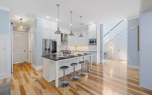 A modern kitchen with white cabinetry, stainless steel appliances, and a central island with bar stools. - Chillville: Pool, Playground & Bikes (Santa Rosa Beach)