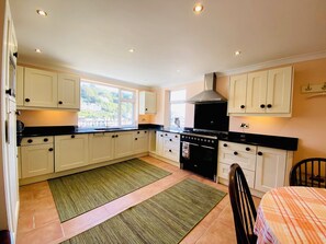 A kitchen with white cabinets, a black stove, and a window overlooking a green landscape. - Harbour Lodge (Looe)