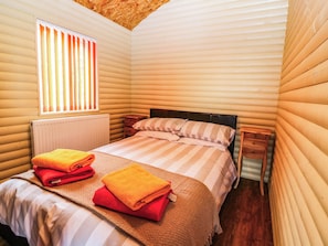 Ein gemütliches Zimmer mit einem Bett, einem Fenster mit Jalousien, einem Heizkörper und einem kleinen Nachttisch.