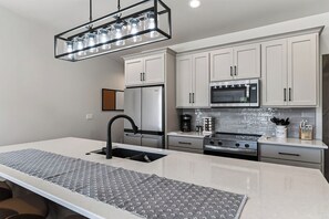 A modern kitchen with white cabinetry, stainless steel appliances, and a central island with a black faucet. - Sturgeon Bay Condo w Marina Slip and in law suite (Sturgeon Bay)
