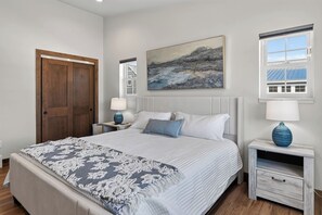 A bedroom with a large bed, a nightstand with a lamp, a dresser, a door, and a painting on the wall. - Sturgeon Bay Condo w Marina Slip and in law suite (Sturgeon Bay)