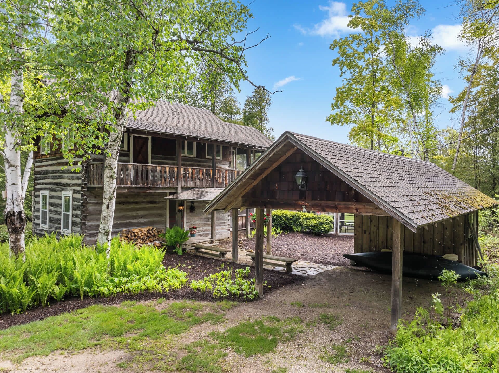 A rustic cabin with a porch and a covered area, surrounded by greenery and trees.
