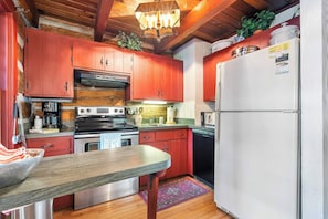 A kitchen with red cabinets, a white refrigerator, a stove, and a wooden dining table. - Nostalgic rustic cabin on Kangaroo Lake-Dog Friendly w/ water access! (Baileys Harbor)