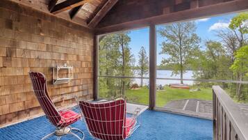 A wooden interior with two red chairs and a table, a large window overlooking a lake and greenery.