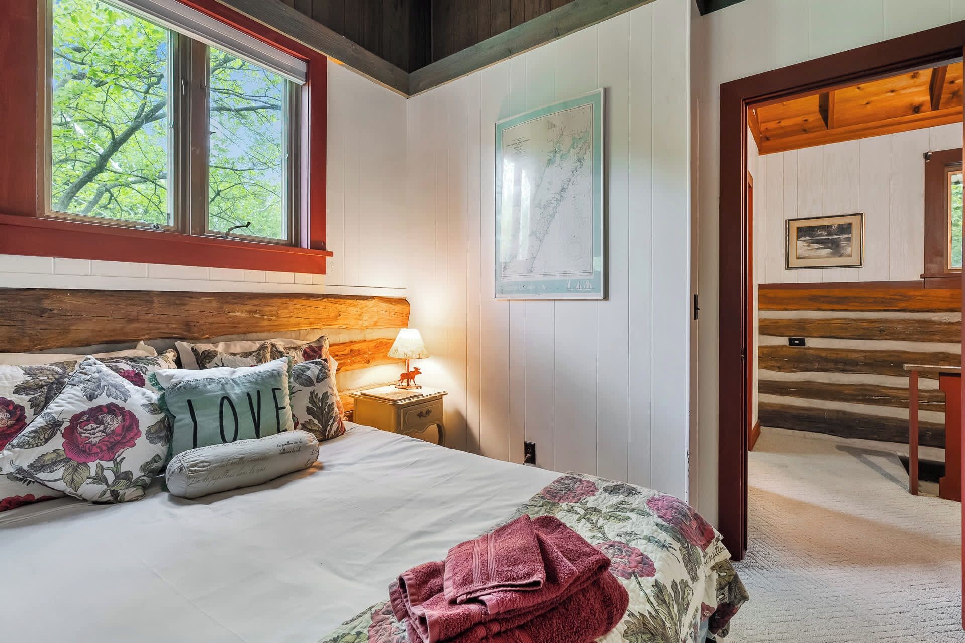 A bedroom with a bed, a nightstand, a lamp, a map on the wall, and a wooden door leading to another room.