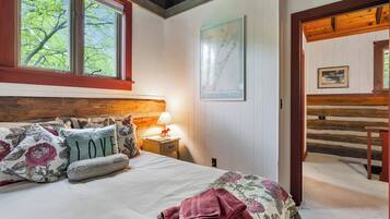 A bedroom with a bed, a nightstand, a lamp, a map on the wall, and a wooden door leading to another room.