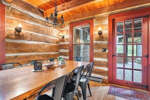 A log cabin interior with a wooden dining table, metal chairs, a chandelier, and a red door with glass panels. - Nostalgic rustic cabin on Kangaroo Lake-Dog Friendly w/ water access! (Baileys Harbor)