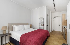 Une chambre moderne avec un lit, des tables de chevet, un miroir et une vue sur la cuisine adjacente.