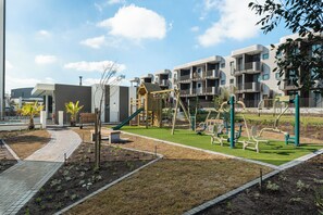 Ein Spielplatz mit Rutsche und Klettergerüsten, umgeben von einer Grünfläche mit Gras und Pflanzen.