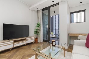 Ein modernes Wohnzimmer mit Flachbildfernseher, Glastisch, Blumentopf und Sofa.