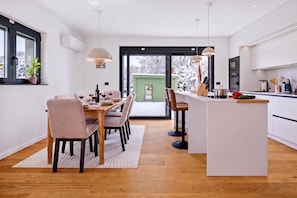 A modern kitchen with a central island, dining area with chairs, and a view through a glass door to a snowy outdoor area. - Green Zone Apartment With Terrace And Parking (Zagreb)