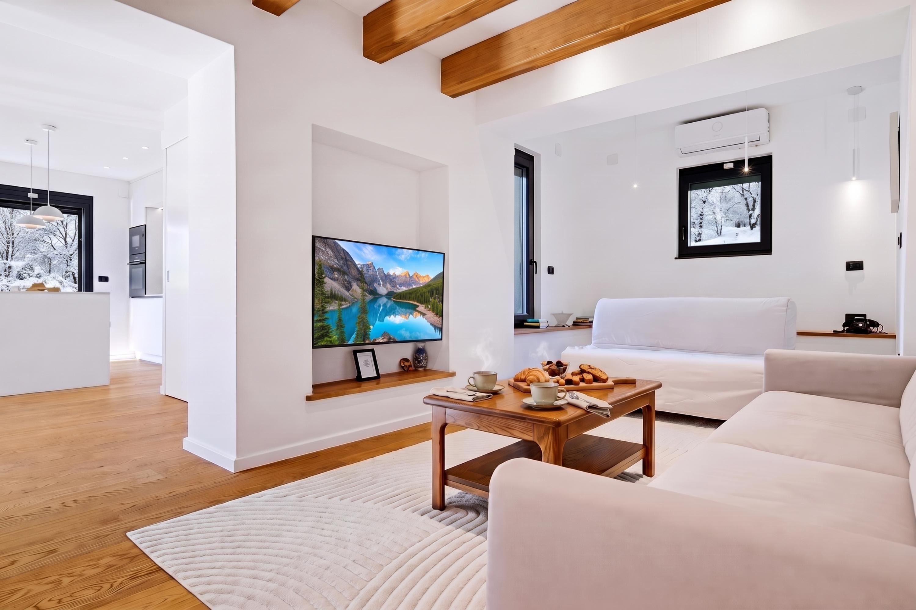 A modern living room with a flat-screen TV, a wooden coffee table with breakfast items, a white sofa, and a large window with a mountain view.