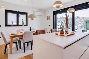 A modern dining area with a central island, pendant lighting, and a view of a snowy landscape through large windows. - Green Zone Apartment With Terrace And Parking (Zagreb)
