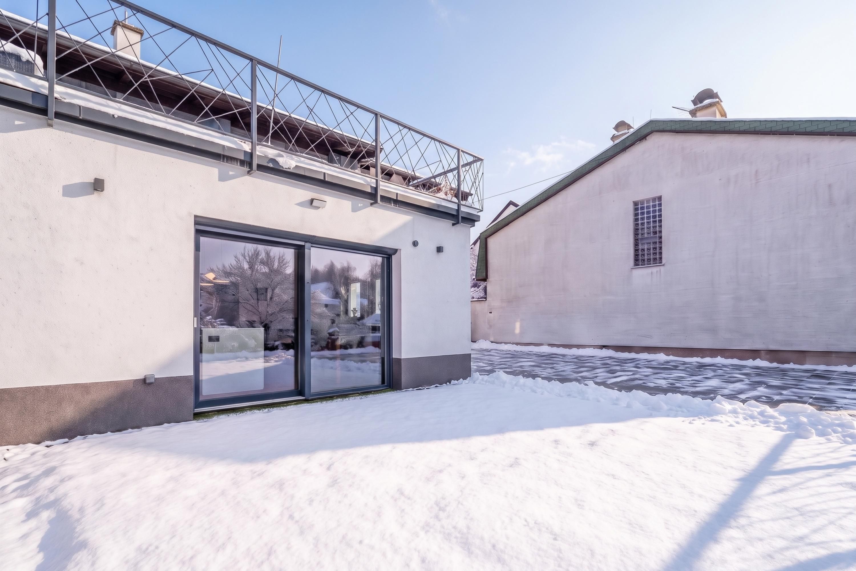 A building with a glass door entrance, a metal balcony, and a snow-covered ground.
