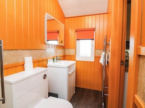 A bathroom with wooden paneling, a white sink, a mirror, and a shower area. - Masons Hut (Berwick-upon-Tweed)