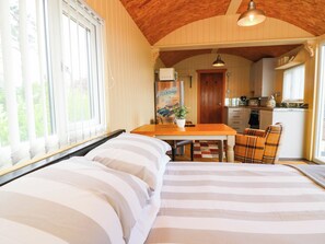 A bedroom with a bed, a dining table with chairs, a kitchen area, and a view of greenery outside. - Masons Hut (Berwick-upon-Tweed)