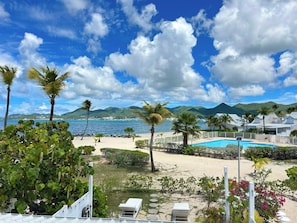 A beach resort with a swimming pool, palm trees, and mountains in the background. - TI PARADISE Studio SXM Baie Nettlé on the Beach (Marigot)