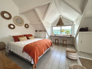 A bedroom with a bed, two stools, a window with a view, and wall decor. - TI PARADISE Studio SXM Baie Nettlé on the Beach (Marigot)