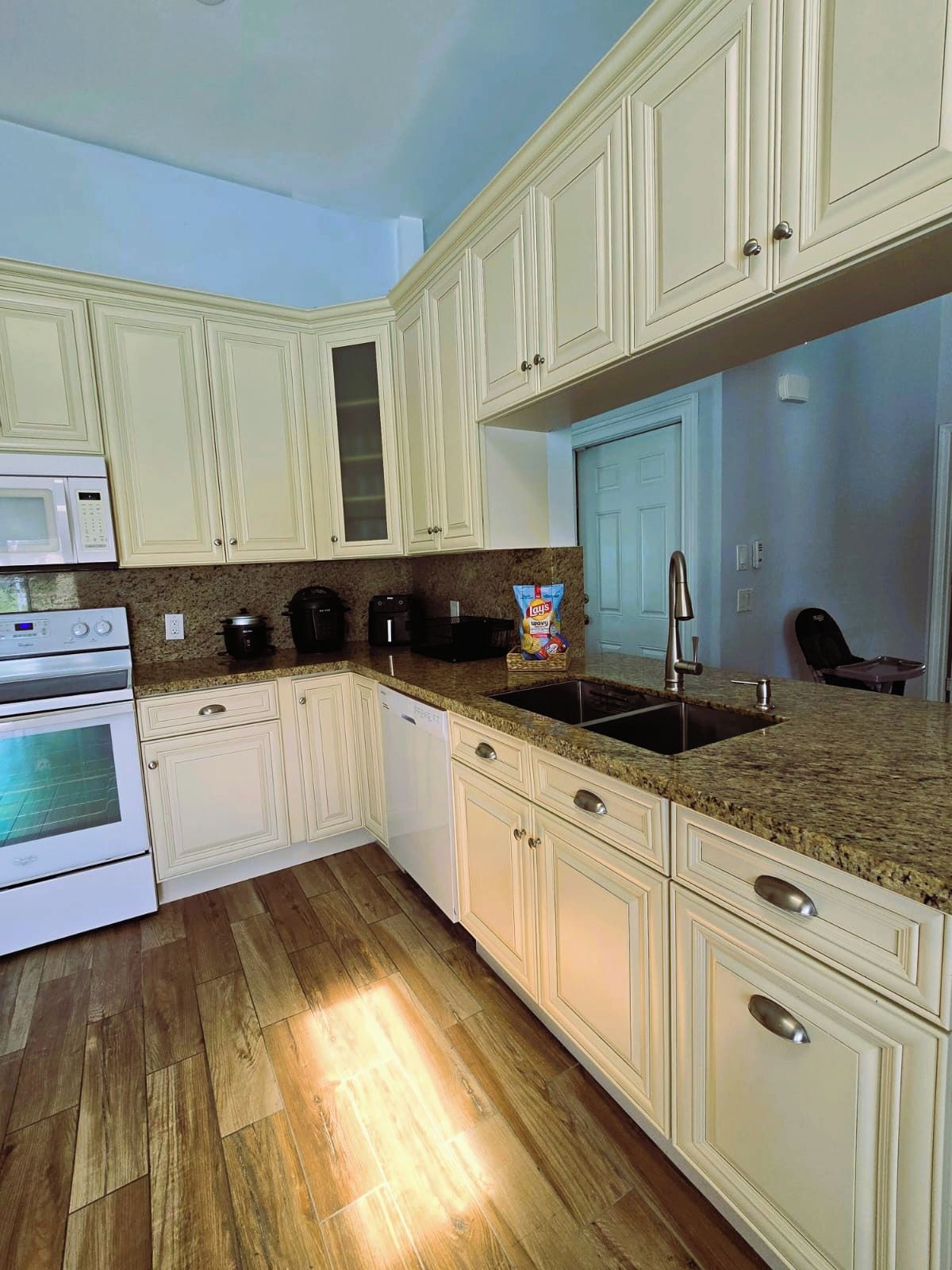 A kitchen with white cabinets, a granite countertop, a stainless steel sink, and a microwave.