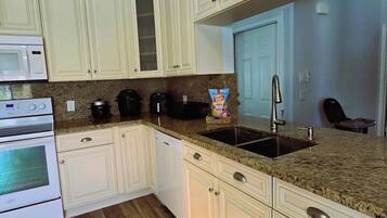 A kitchen with white cabinets, a granite countertop, a stainless steel sink, and a microwave.