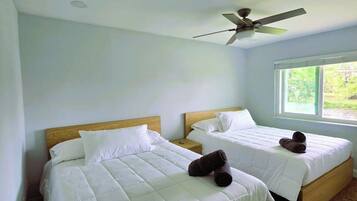 A hotel room with two beds, a ceiling fan, and a window with a view of greenery.