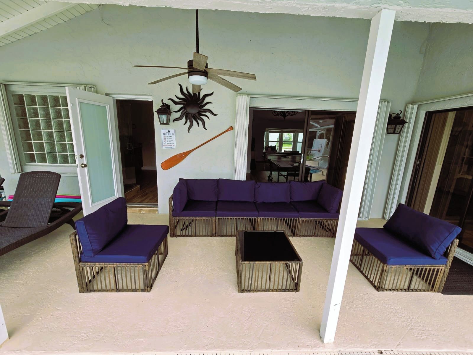 A covered outdoor seating area with a ceiling fan, a wall-mounted bat decoration, and a pool rules sign.