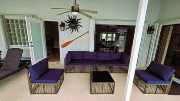 A covered outdoor seating area with a ceiling fan, a wall-mounted bat decoration, and a pool rules sign.