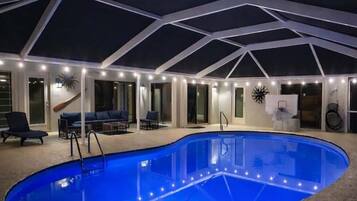 An indoor swimming pool with a glass enclosure, surrounded by a lounge area with seating and a ceiling with a geometric design.