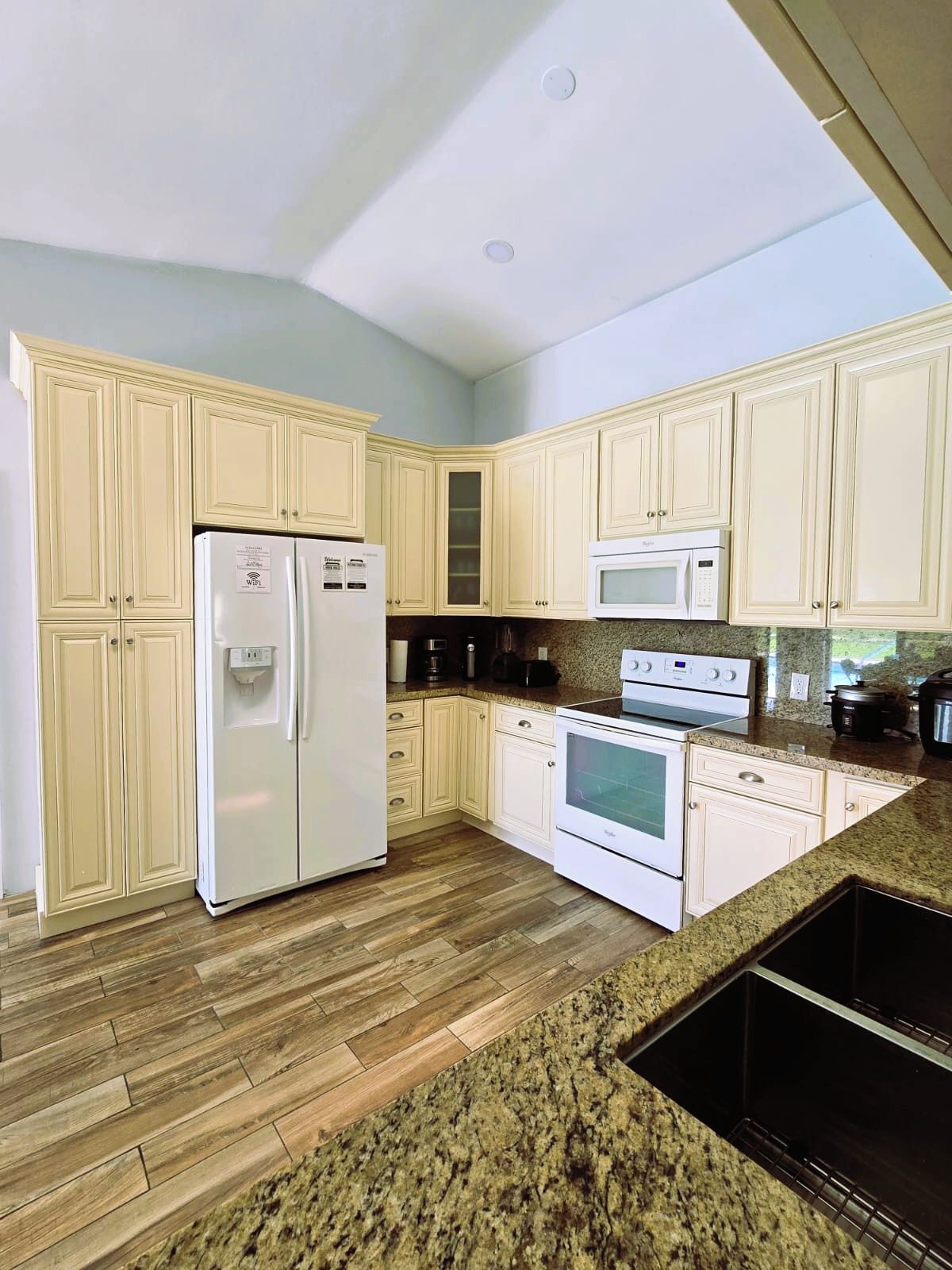 A kitchen with white cabinets, a refrigerator, a microwave, an oven, and a granite countertop.