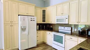 A kitchen with white cabinets, a refrigerator, a microwave, an oven, and a granite countertop.