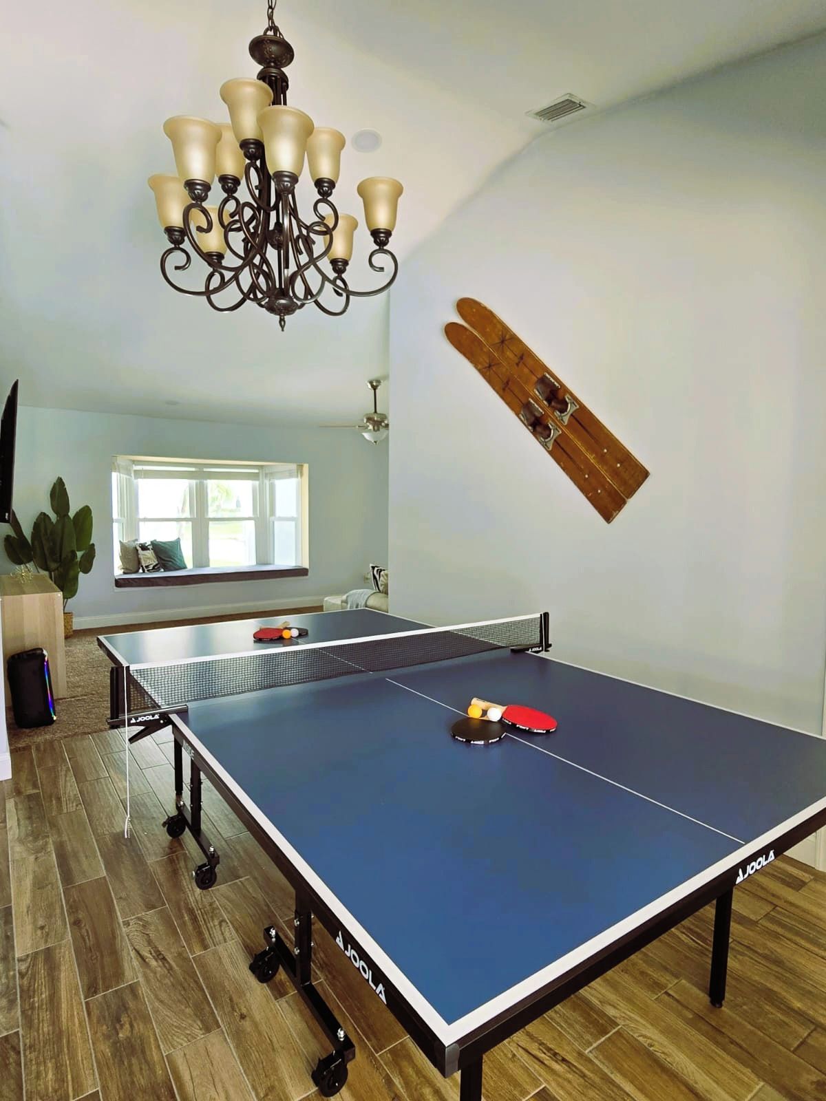 Una mesa de ping pong con un ventilador de techo y una araña en una habitación con suelo de madera.